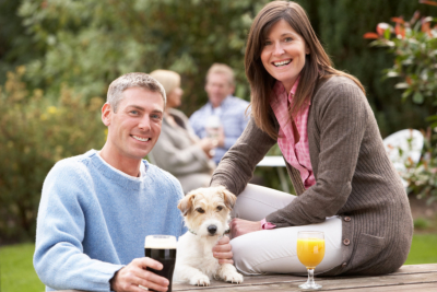 Couple With Pet Dog Outdoors Enjoying Drink In Pub Garden